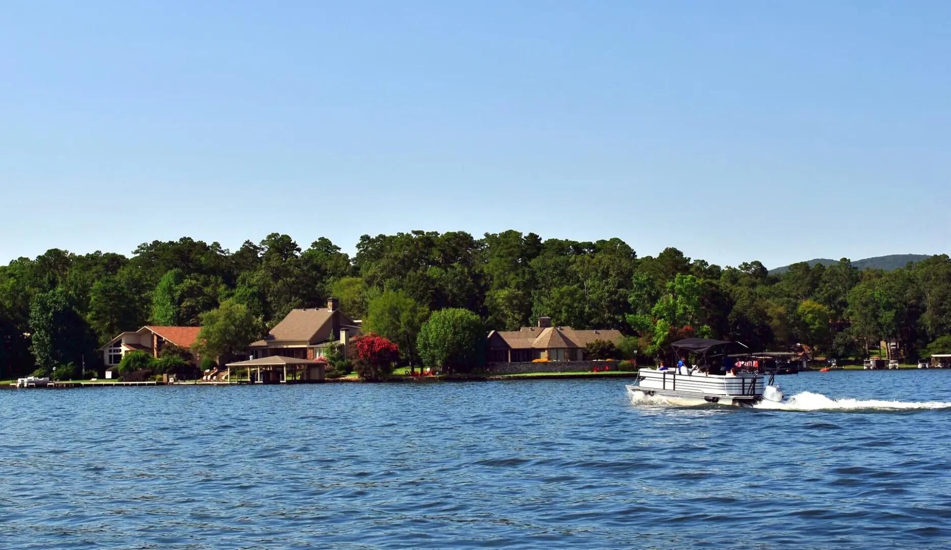 Beautiful scenic view of lake houses on the shoreline with a pontoon boat in the water.