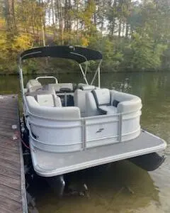 White pontoon boat docked at a lake.