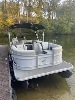 White pontoon boat docked at a lake.