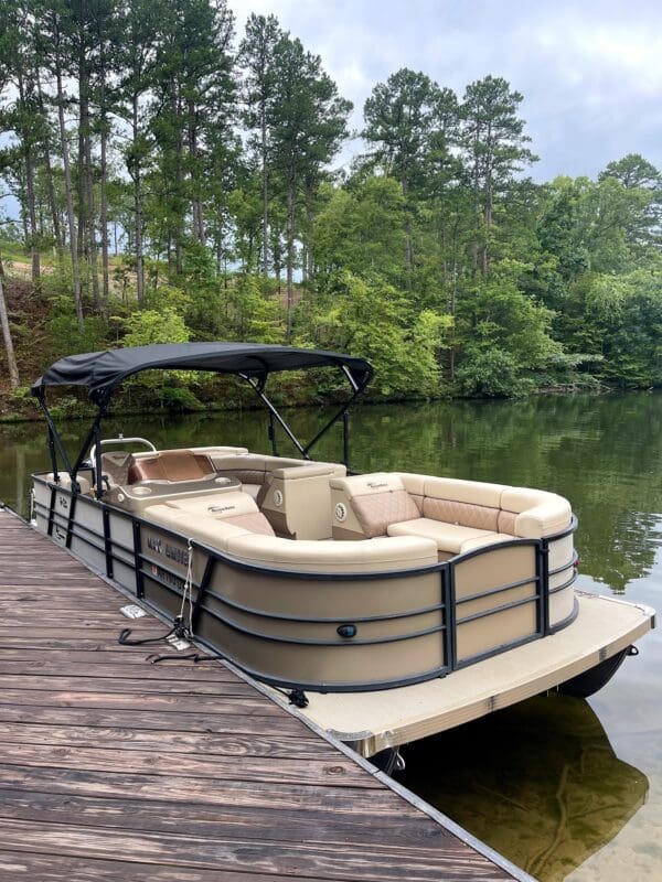 Tan pontoon boat docked at a lake.